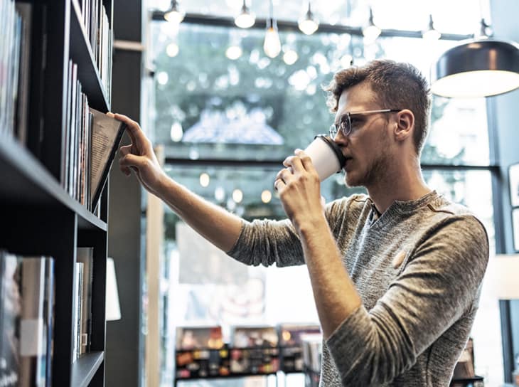 Adult man browsing in library stacks while drinking a cup of coffee