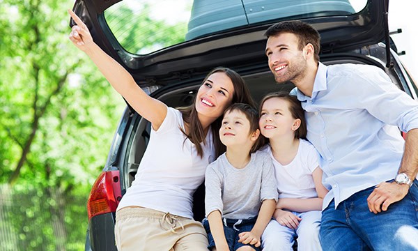 Young family on vacation sitting in the back of their SUV enjoying springtime weather