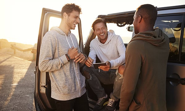 Three male friends gathered around SUV and talking