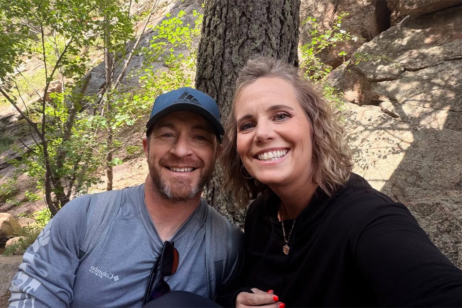 a couple sitting outside in the woods smiling