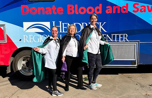 three employees standing in front of the Blood Drive bus