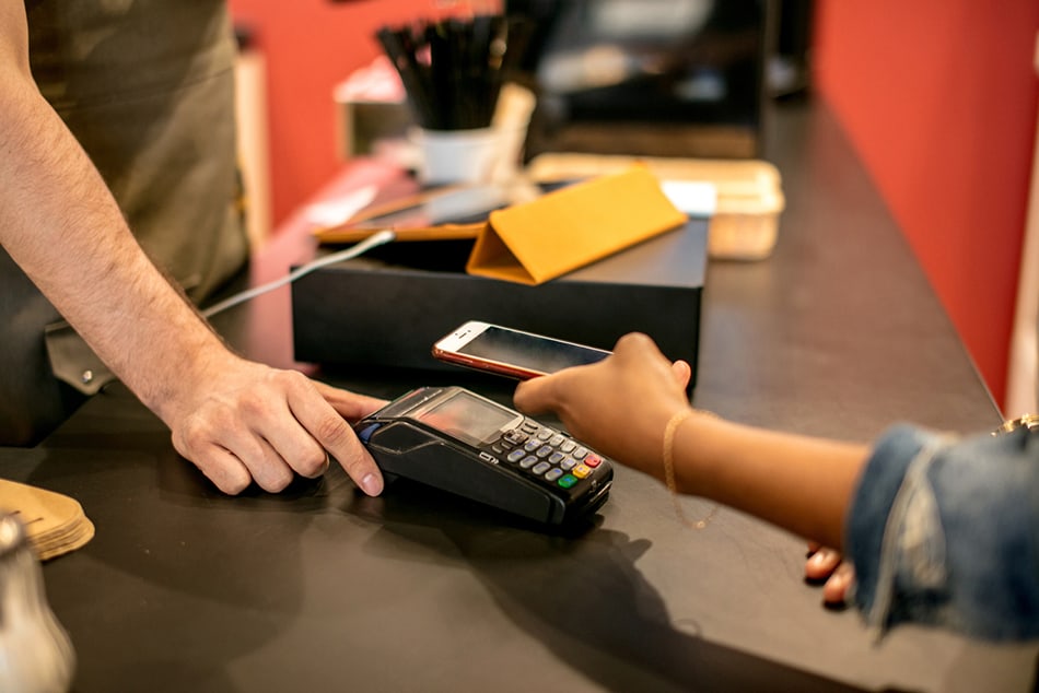 Man holding iPhone to make a contactless payment at check out