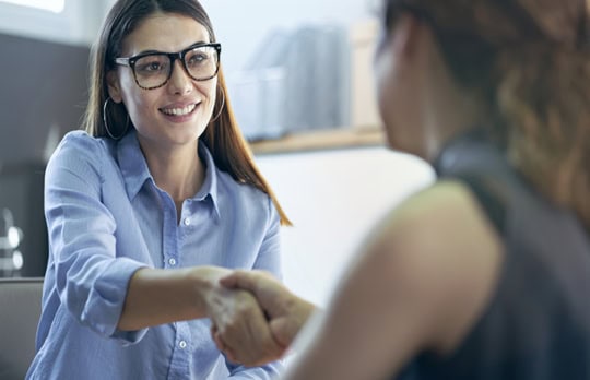 Young, casually dressed female employee shaking hands with a member