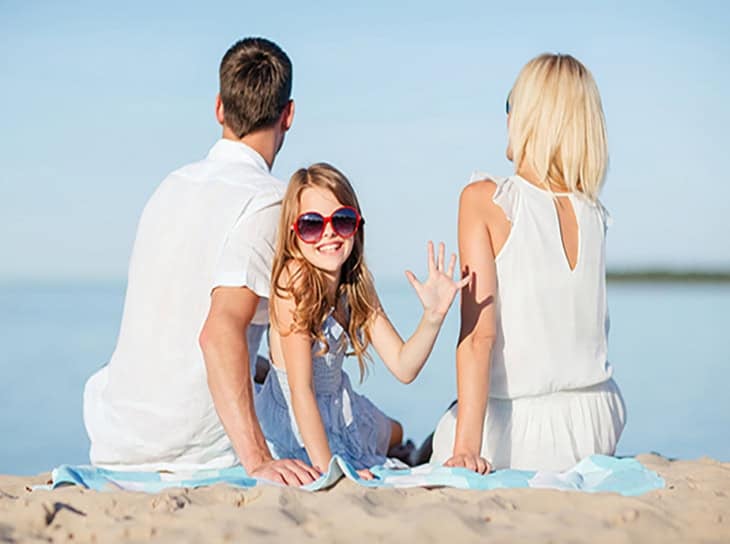 Mom, dad and young child on a beach. The child has turned around to wave at the photographer.