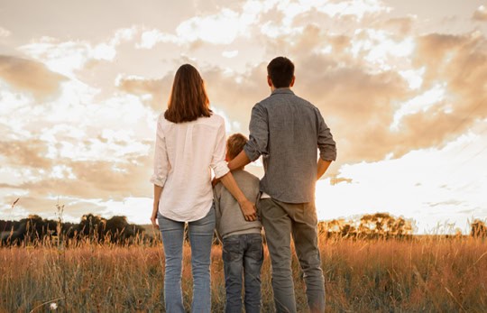 Family of three standing in a meadow and watching the sunrise.