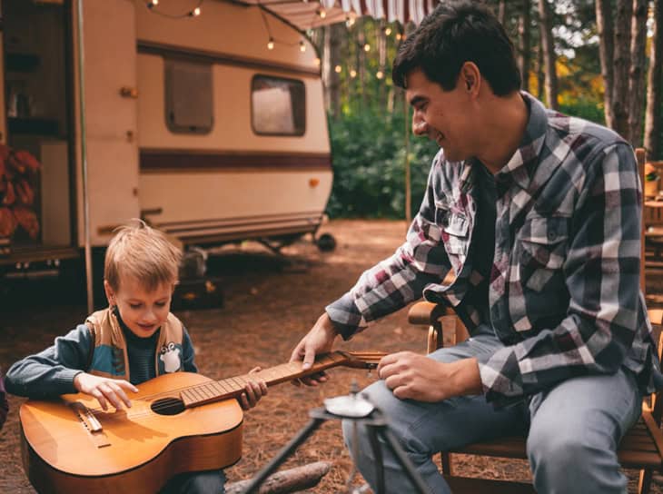 Father teaches his son to play guitar while on a camping trip in the forest.