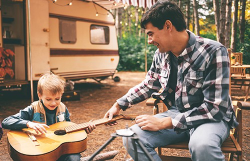 Father teaching guitar to his son on a camping trip