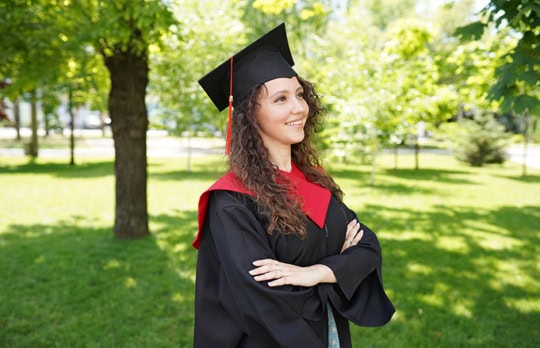 Picture of female high school graduate wearing graduation robe and standing in a park