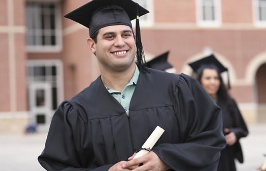 Male graduate in cap and gown in front of a red brick building