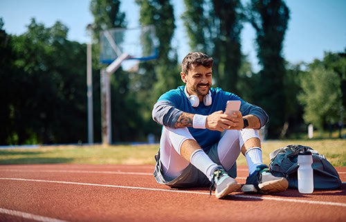 Male jogger checking his smart phone while taking a break from running