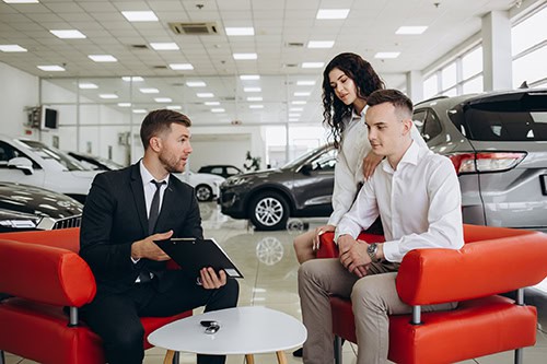 Young adult couple talking to salesman at an auto dealership