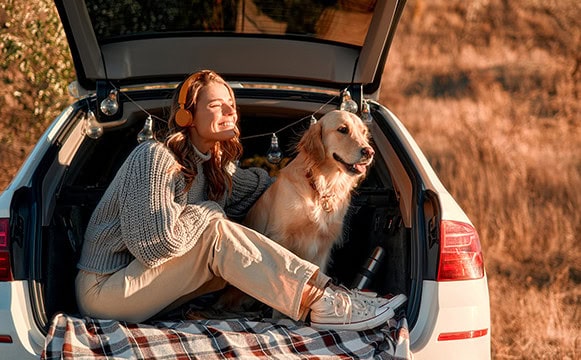 Young woman and her dog enjoying autumn weather in the hatchback section of her car