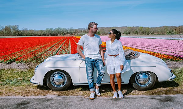 Young couple in front of a vintage convertible on vacation in the tulip fields of the Netherlands