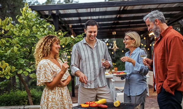 Group of different aged friends enjoying an outdoor dinner in front to backyard pavilion.