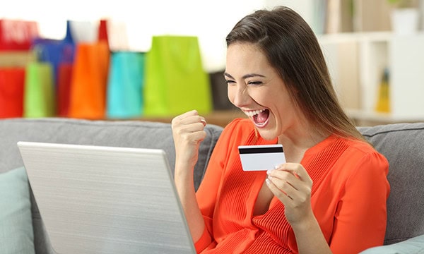 Excited woman holding credit card and viewing display on a laptop computer
