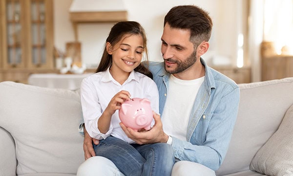 Father and daughter depositing money into piggy bank
