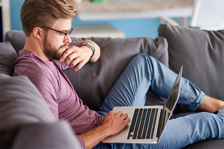 Man stretched out on couch working on laptop