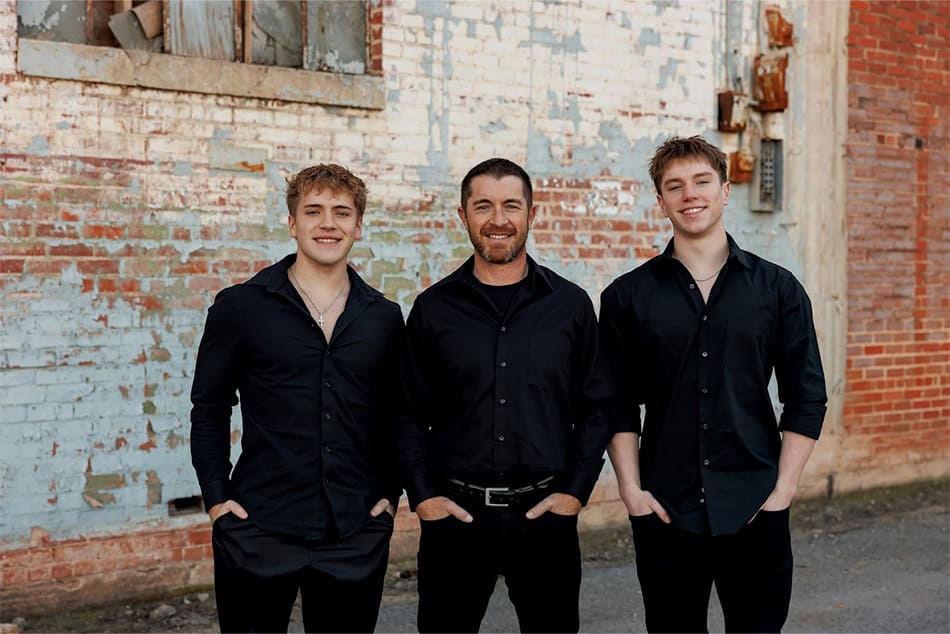 A DAD WITH HIS TWO SONS IN FRONT OF A BRICK WALL