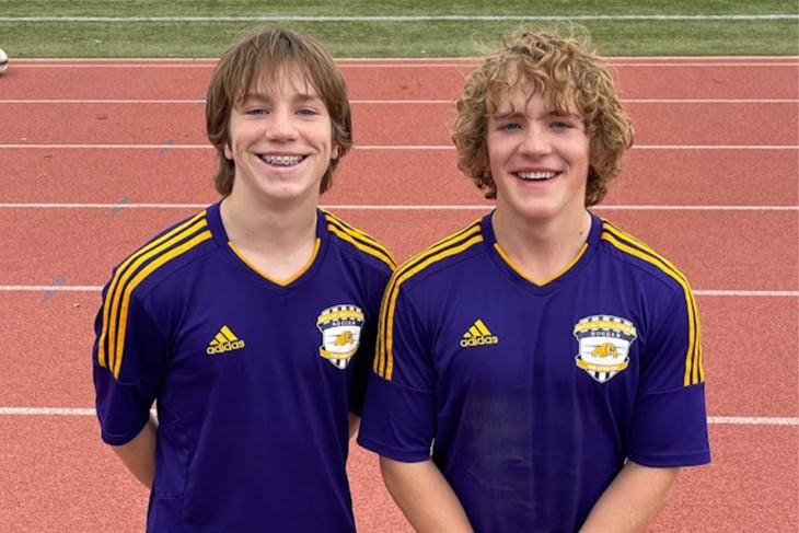two boys in soccer uniforms standing on a track