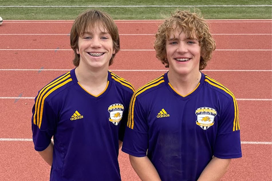 two boys in soccer uniforms standing on a track