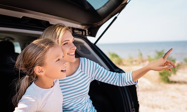 Mother and young daughter sitting in the back of their SUV at the beach.
