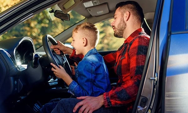 Father letting his young son hold the steering wheel of a pick up truck