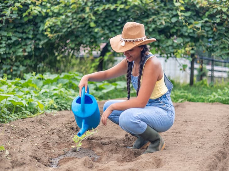 Young woman in straw hat and overalls watering new plants