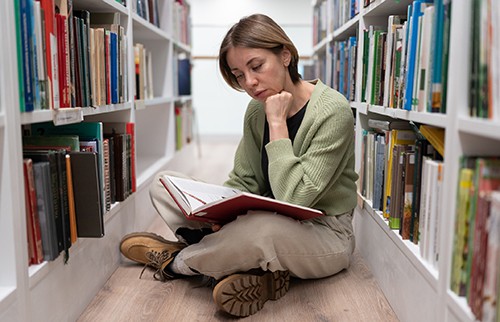 Woman reading a book between the stacks in a library