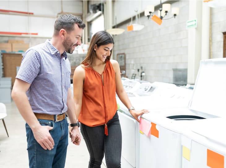 smiling couple holding hands while looking at price of washing machine